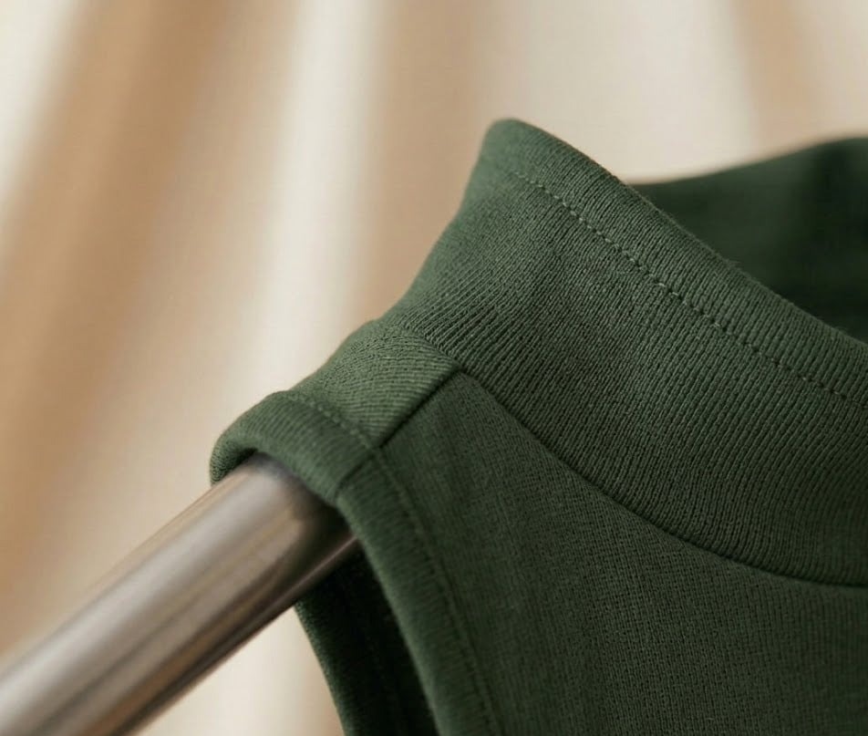 Forest green sleeveless golf top on a brushed metal rack against draped cream fabric